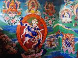 33 Paintings Outside Cave Of The Female Yak Horns Dirapuk Gompa Lion-Faced Goddess Dakini Simhamukha Senge Dongma, Padmasambhava Guru Rinpoche, Milarepa, Marpa, Shangpa Karpo, Shri Devi Palden Lhamo At the back of the Dirapuk Gompa is the cave of the female yak horns. Murals surround the entrance including the lion-faced-goddess Dakini Simhamukha (Tib. Senge Dongma). The face is a white lion with three round orange eyes blazing fiercely with a gaping mouth, and hair flowing upward. The right hand holds upraised a curved knife to the sky, left a skullcup of blood to the heart, carrying a khatvanga staff tipped with a trident in the bend of the elbow supported against the shoulder. Above to the left is Buddha, then Chakrasamvara (Tib. Demchog) in yab-yum with Vajrayogini (Tib. Dorje Phagmo), Padmasambhava (Tib. Guru Rinpoche), Milarepa holding his hand to his ear, Milarepa�s teacher Marpa, At the lower left is the worldly protector Shangpa Karpo, white, with one face and two hands holding a lance in the right and a bowl of jewels in the left; riding a white horse. I�m not sure who the figure is to the right of lion-faced goddess. He is white with one face and two hands holding upraised in the right a riding whip and in the left a spear with a red banner. The final figure to the lower right is Shri Devi (Tib. Palden Lhamo), dark blue in colour, riding side saddle on a white mule with a sword in her upper right, a skullcup in her lower right, and khatvanga in her first right hand and another staff in her far right hand. She has a sun and moon disc at her waist.